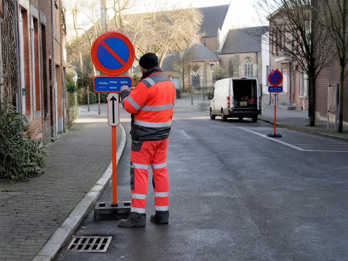 Medewerker controleert het onderbord van een parkeerverbodsbord bij het dorpsplein in Mariakerke