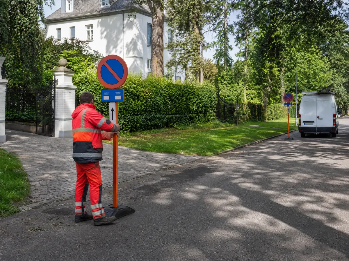 Medewerker plaatst een parkeerverbodsbord in een groene villadreef in Schoten